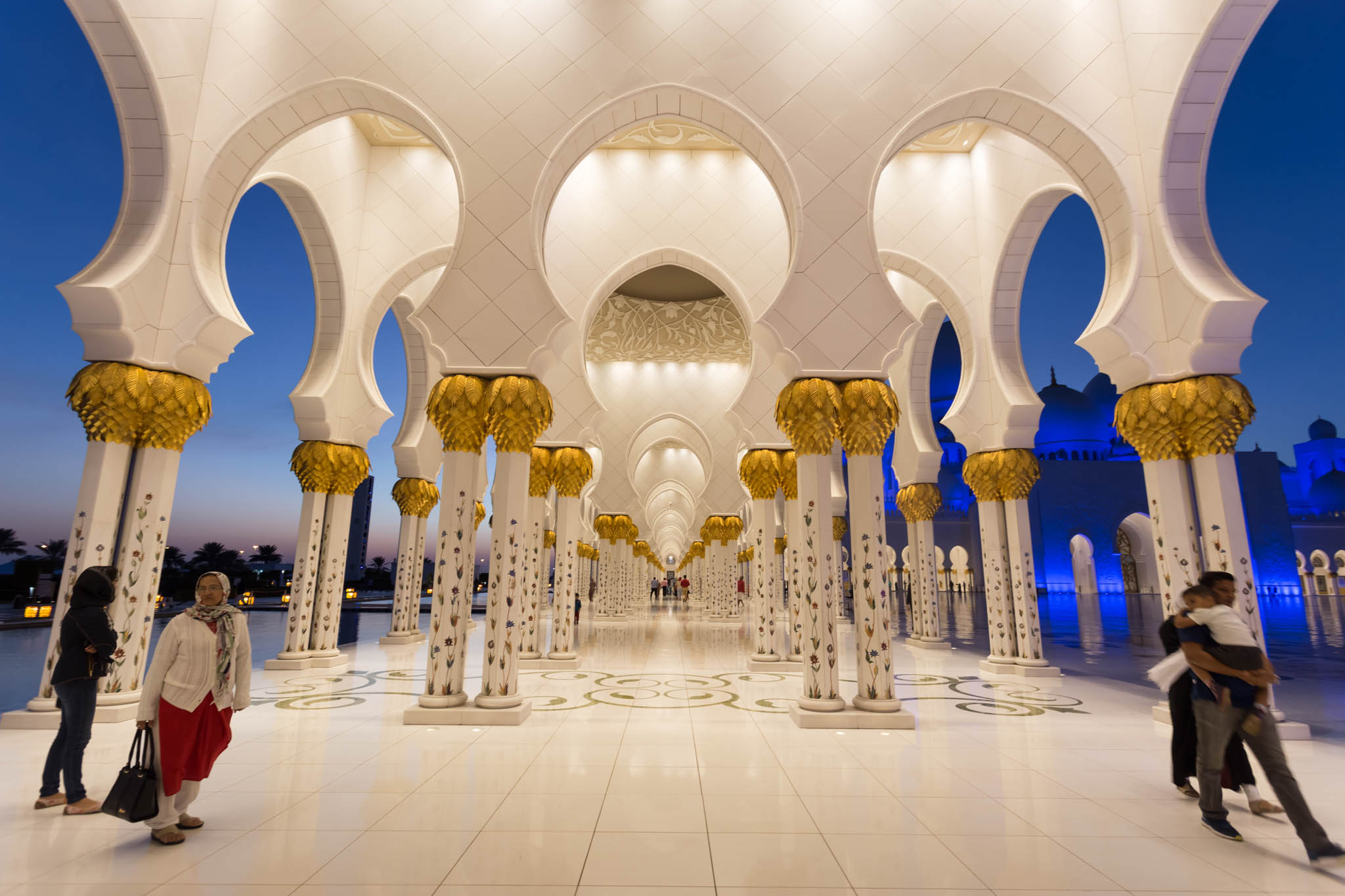 a white and gold building with arches and columns with Sheikh Zayed Mosque in the background