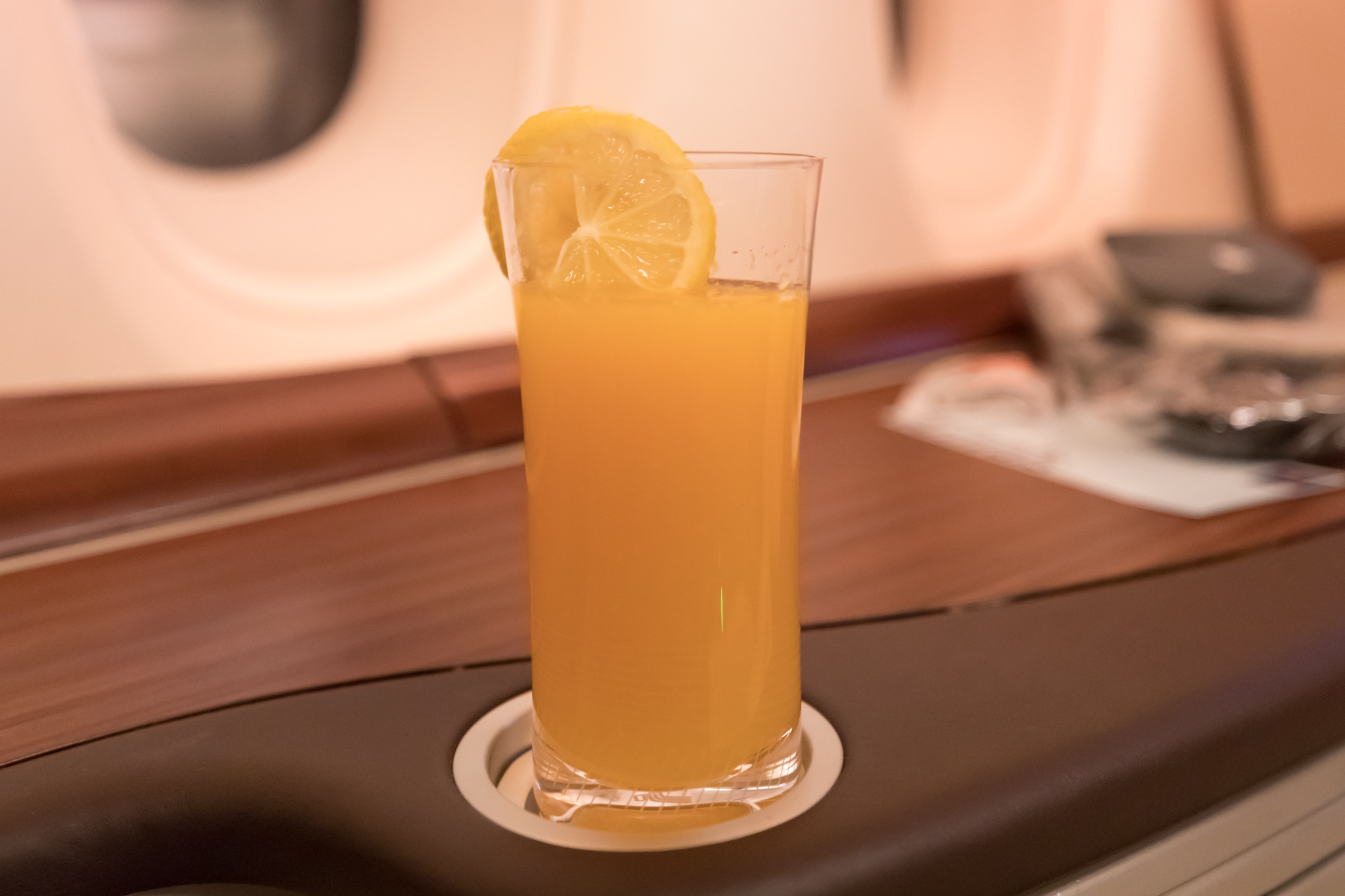 a glass of orange juice with a slice of lemon on a coaster