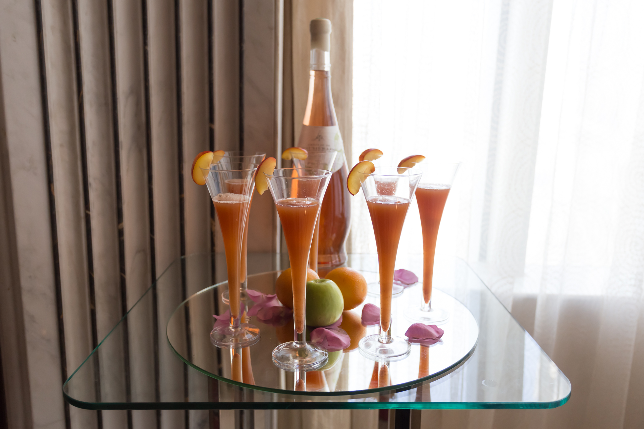 a group of glasses with orange liquid and fruit on a glass table