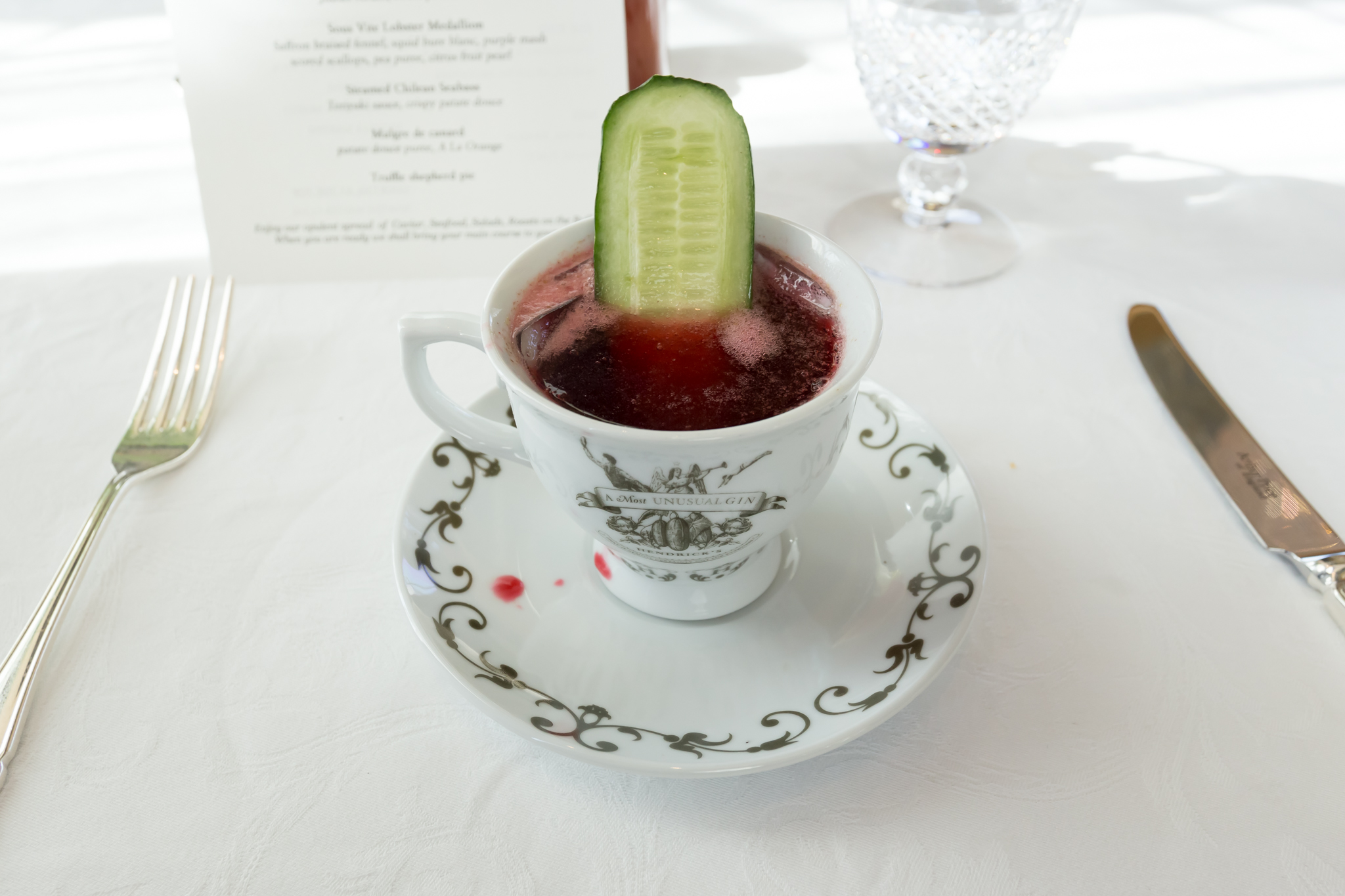 a cup of red liquid with a cucumber slice on top