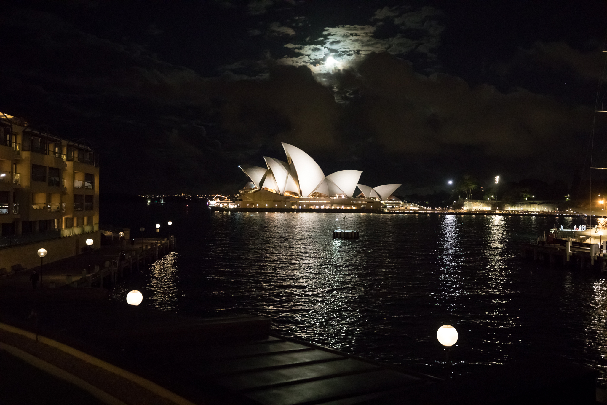a building with white sails on it and a body of water with a moon in the background