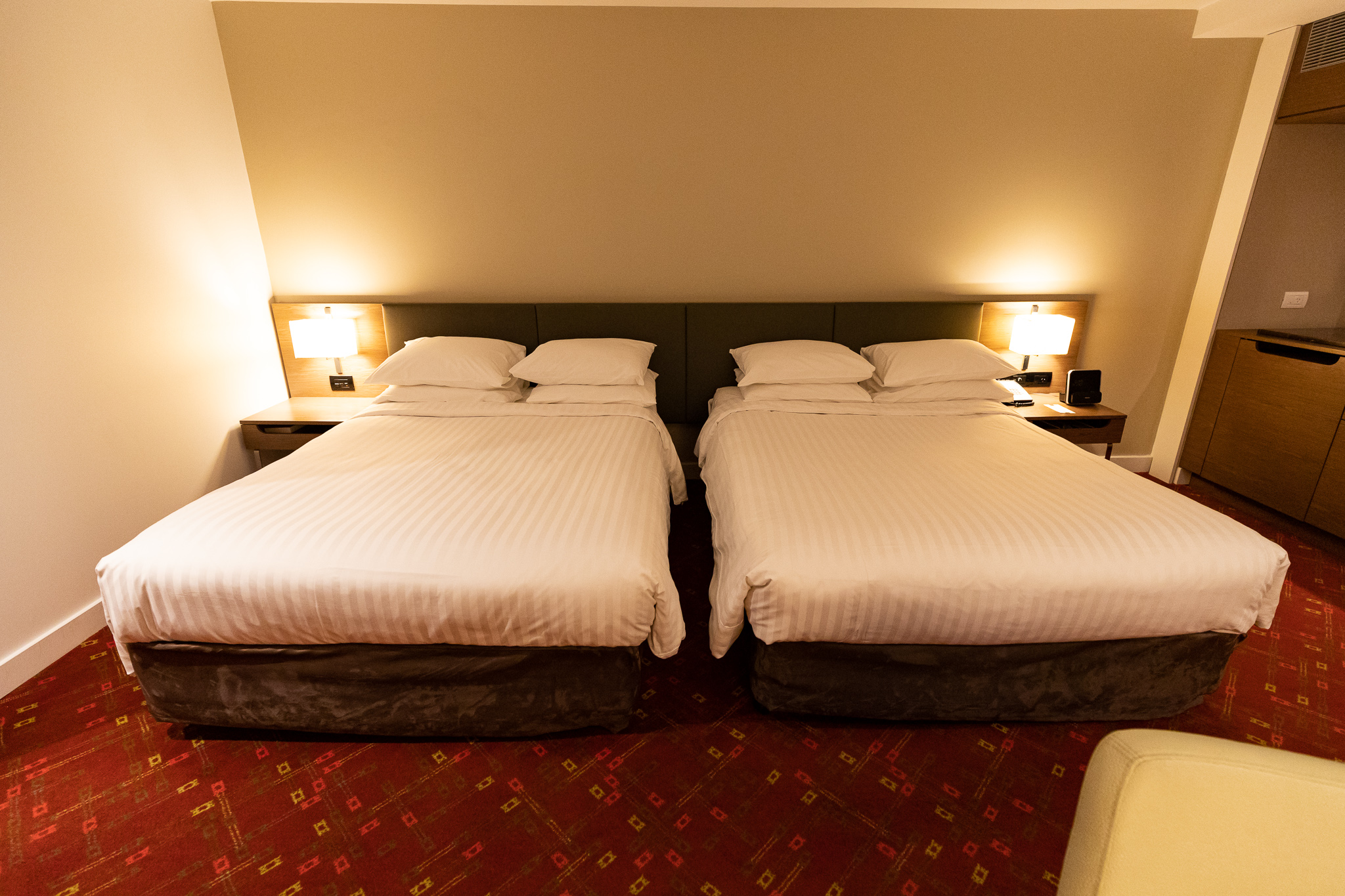 two beds with white sheets and pillows in a room with red carpet