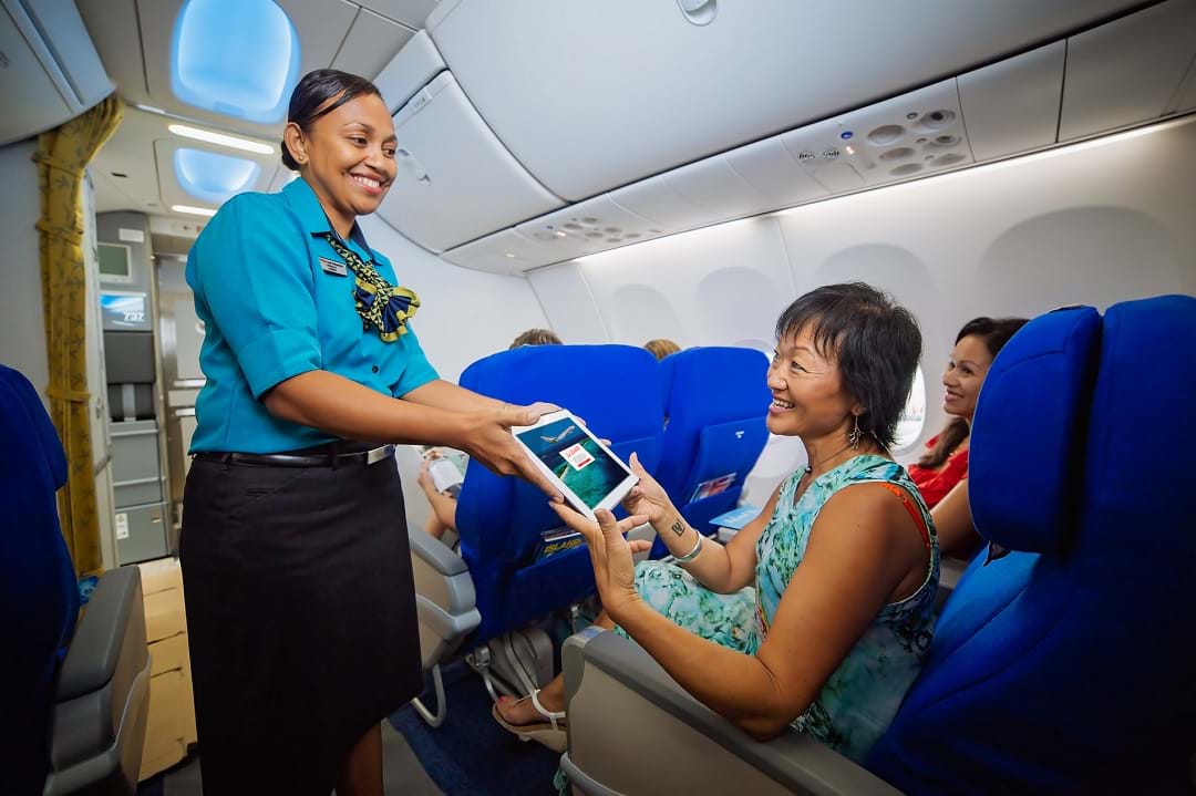 a woman giving a tablet to a woman on an airplane
